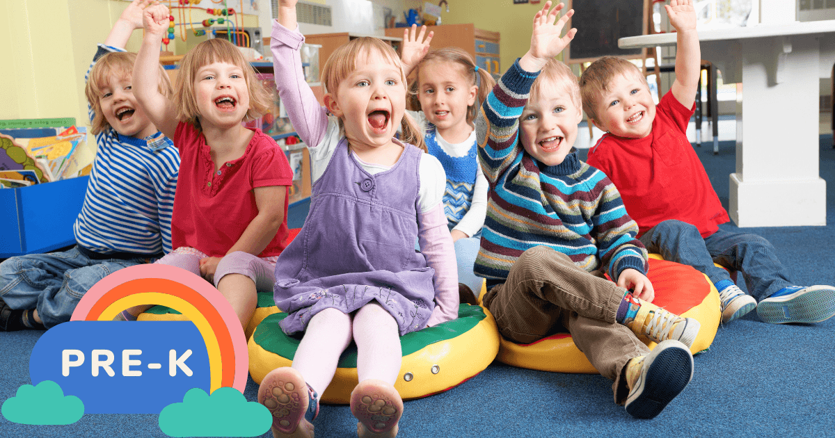 Six young children sit on colorful cushions in a cheerful classroom, smiling and raising their hands. A graphic with a rainbow and the words PRE-K is in the lower left corner—perfect for those searching for Pre-K near me.