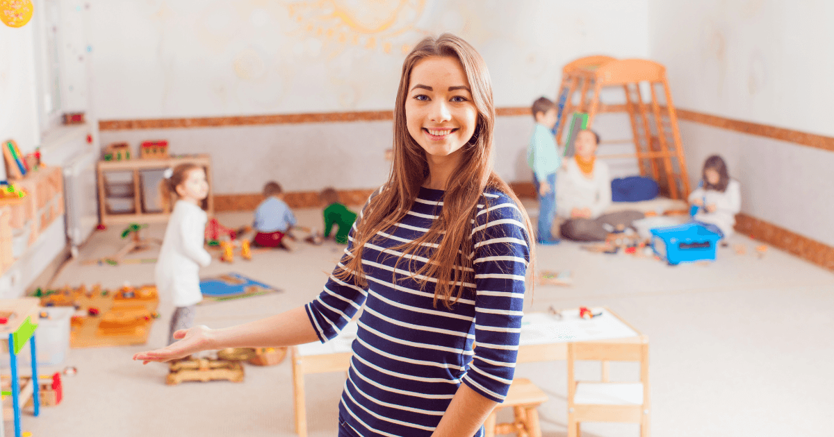 A woman in a striped shirt smiles and gestures toward a Waldorf classroom, where several children play with toys and blocks amid bright, cheerful decorations designed for young kids.