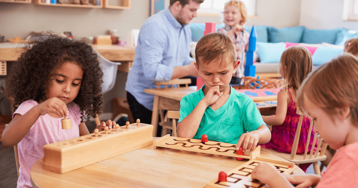 Children sit at a table in a classroom, concentrating on wooden educational puzzles, reflecting environments where parents wonder, "Is Montessori worth it?" The cozy, colorful room is filled with children and an adult engaging in activities.