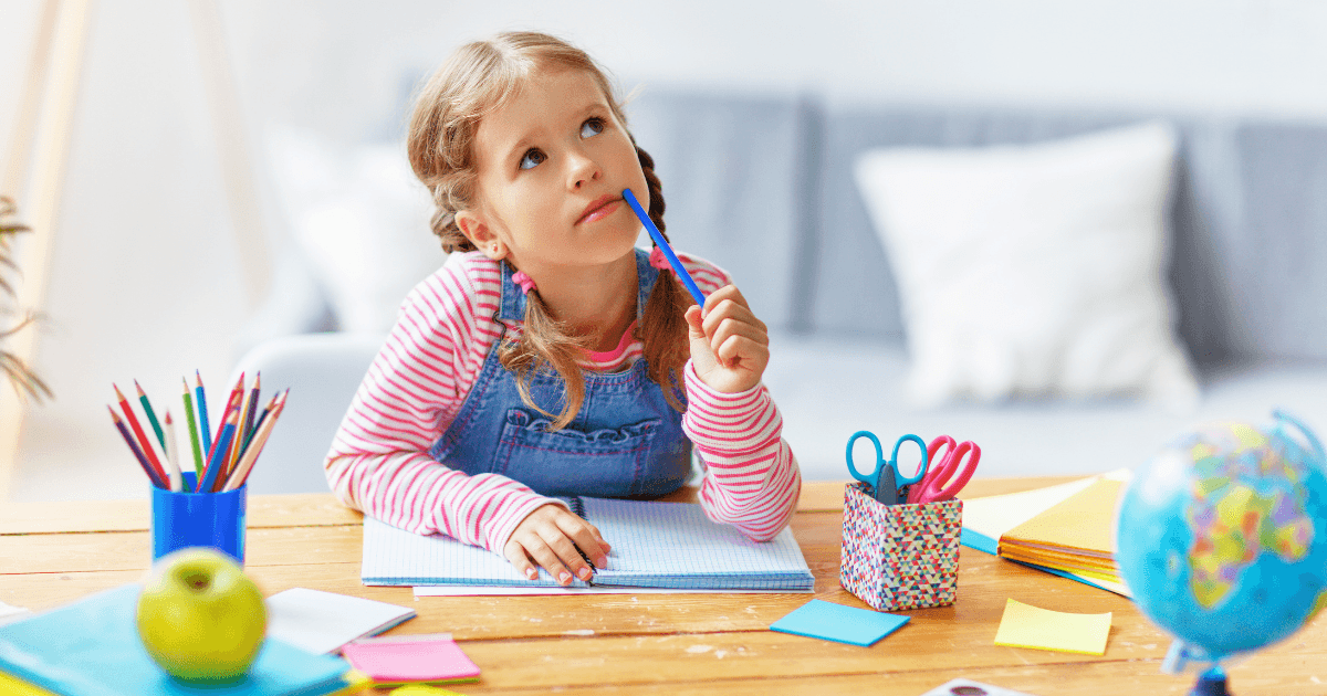 A young girl with braided hair sits at a desk, holding a pencil to her chin and looking up thoughtfully. The desk is covered with colorful school supplies, notebooks, and a small globe—perfect for creating child portfolios.