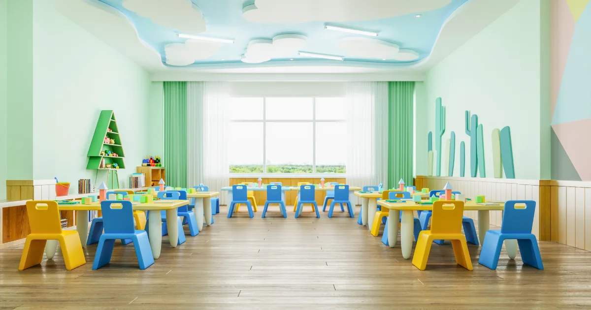 A bright, colorful classroom with small blue and yellow chairs around white tables showcases thoughtful classroom organization. Toys and books are on shelves against pastel green walls, while large windows and playful cloud designs create a cheerful atmosphere.