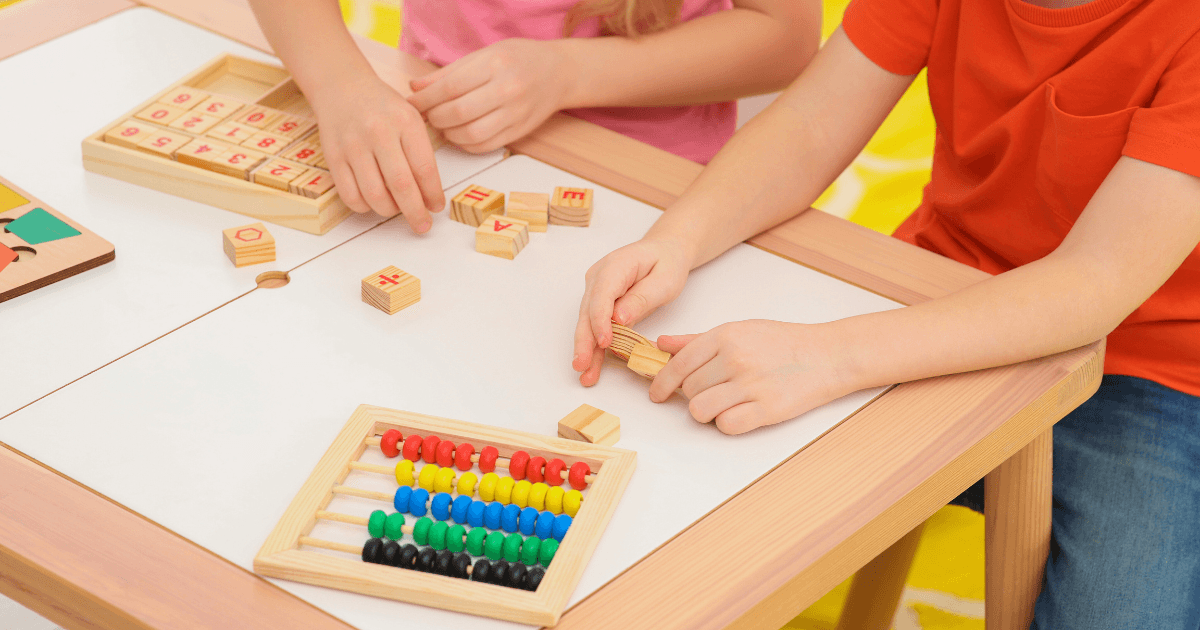 Two children sit at a table playing with educational wooden toys, including letter blocks and a colorful abacus from home learning kits, engaging in hands-on learning activities.