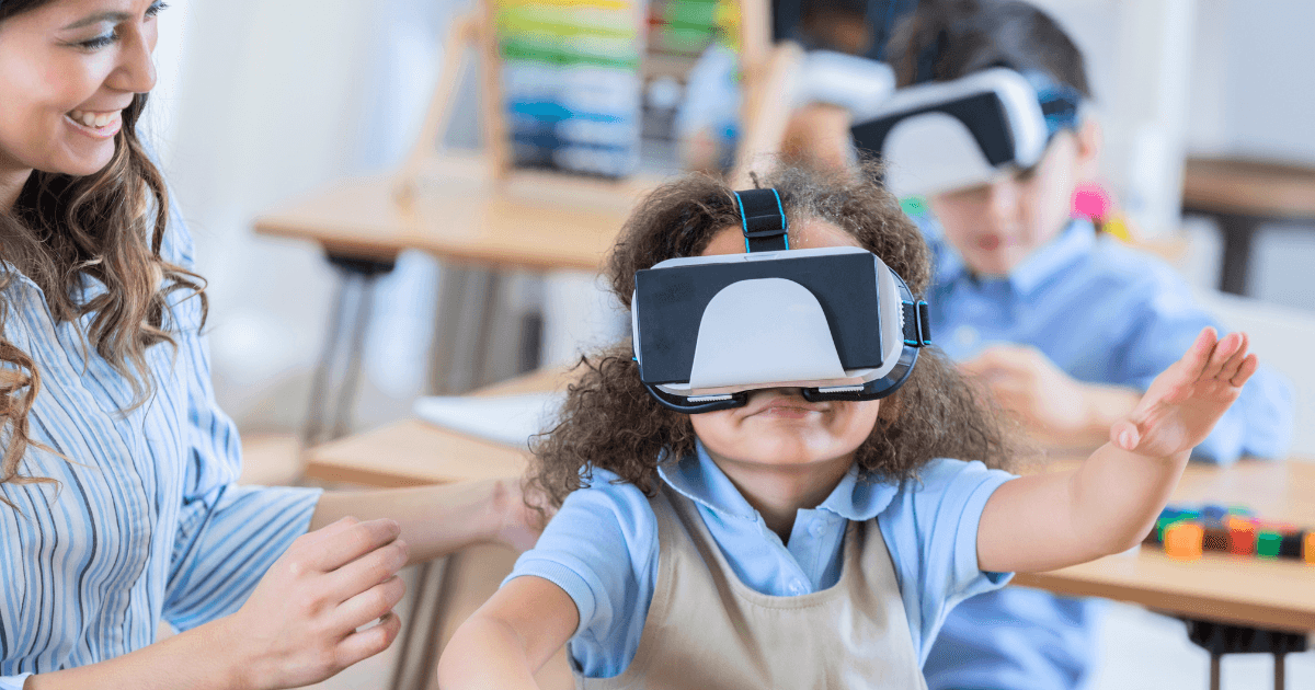 A young girl wearing a virtual reality headset raises her arms in a classroom, while a smiling teacher assists her. Other children in the background join immersive virtual field trips and interact with educational activities.